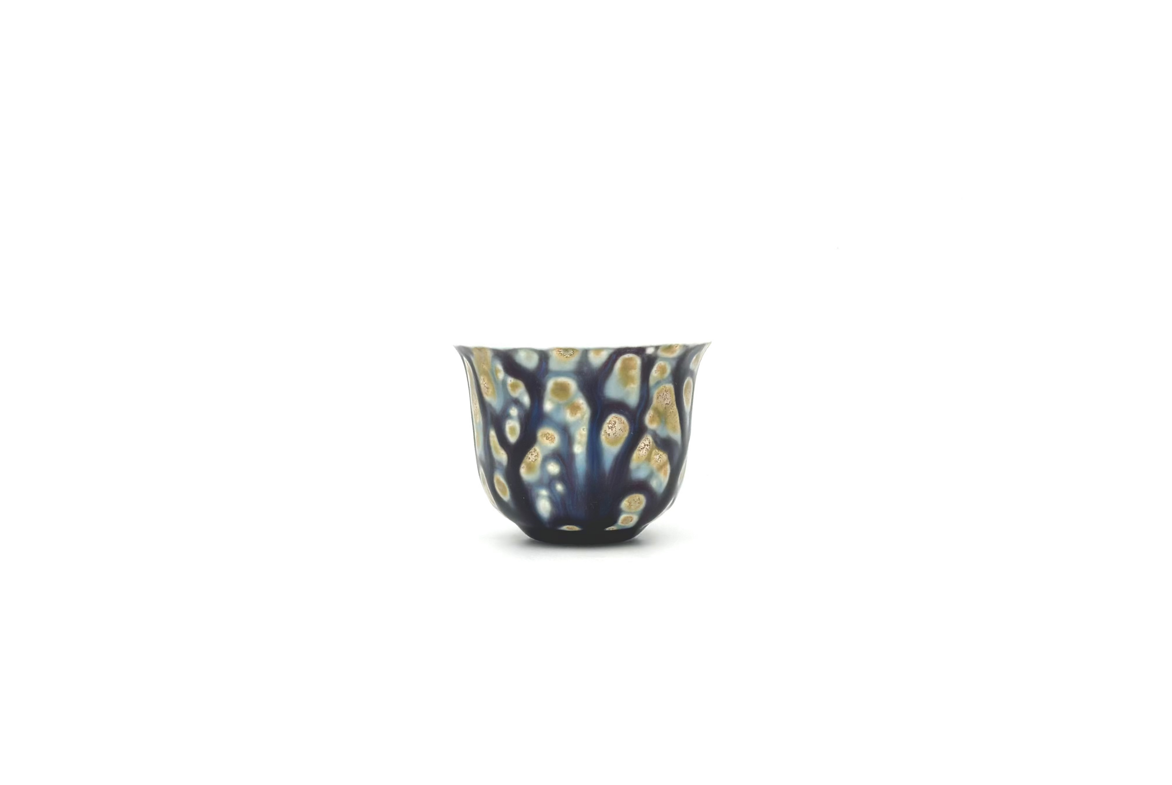 Small ceramic cup with a blue and gold pattern on a white background