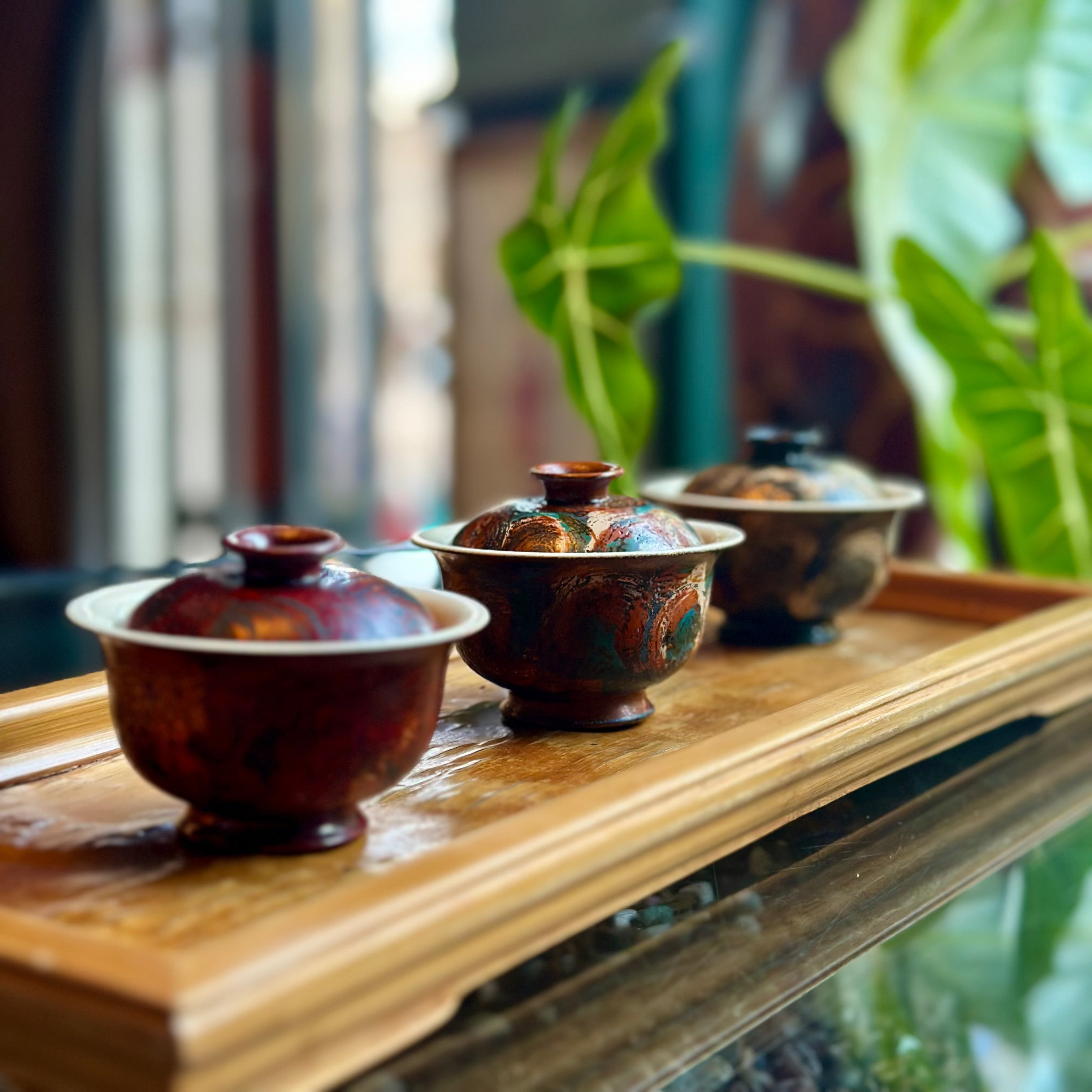 Three ceramic teapots on a wooden tray with a blurred indoor background
