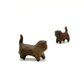 A close-up studio shot of a handcrafted Yixing clay cat tea pet in sharp focus in the foreground, with a second cat tea pet softly blurred in the distant corner, all set against a pure white background.