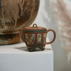 Close-up Cloud & Thunder Yixing teapot standing next to a wabi-sabi style vase, highlighting the intricate hand-painted geometric fretwork.
