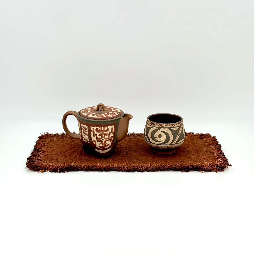 Studio shot of the Cloud & Thunder motif Yixing Zisha teapot paired with a matching teacup, resting elegantly on a textured tea mat.