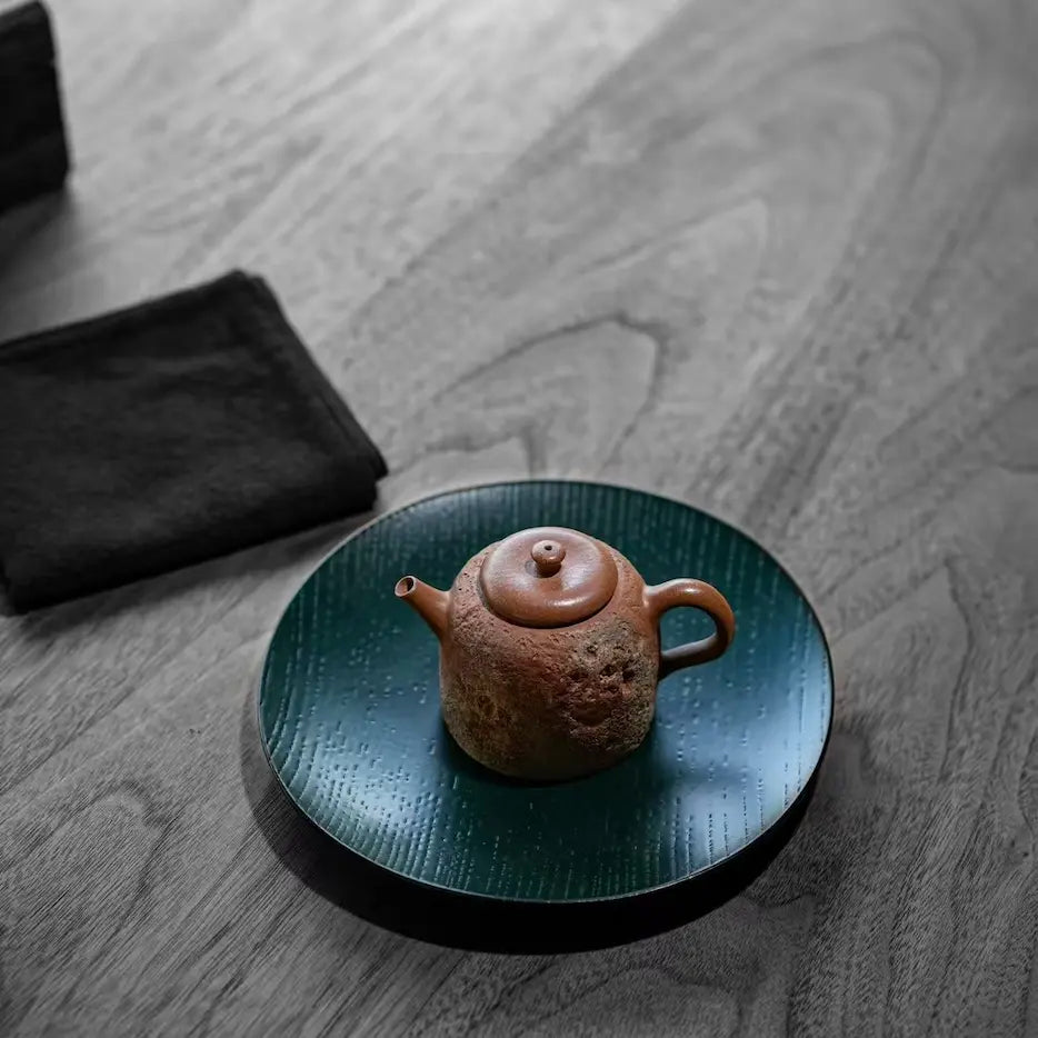 High-angle lifestyle view of the Desert Mirage hand-painted Yixing teapot resting elegantly on a dark wood lacquer tea boat atop a modern tea table.