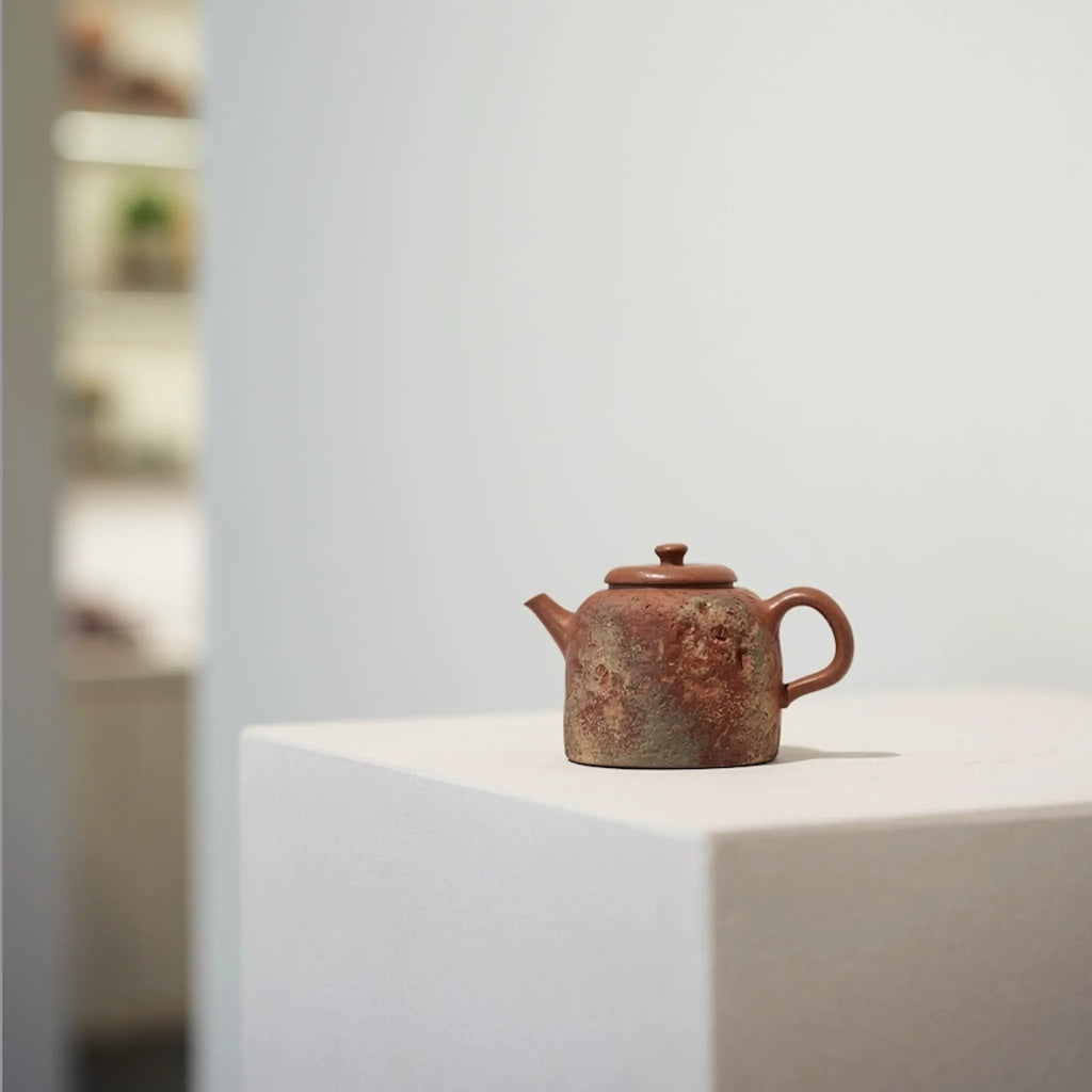 The Desert Mirage painted Yixing Zisha teapot displayed as a work of art, sitting on a minimalist white stand in a contemporary gallery setting.