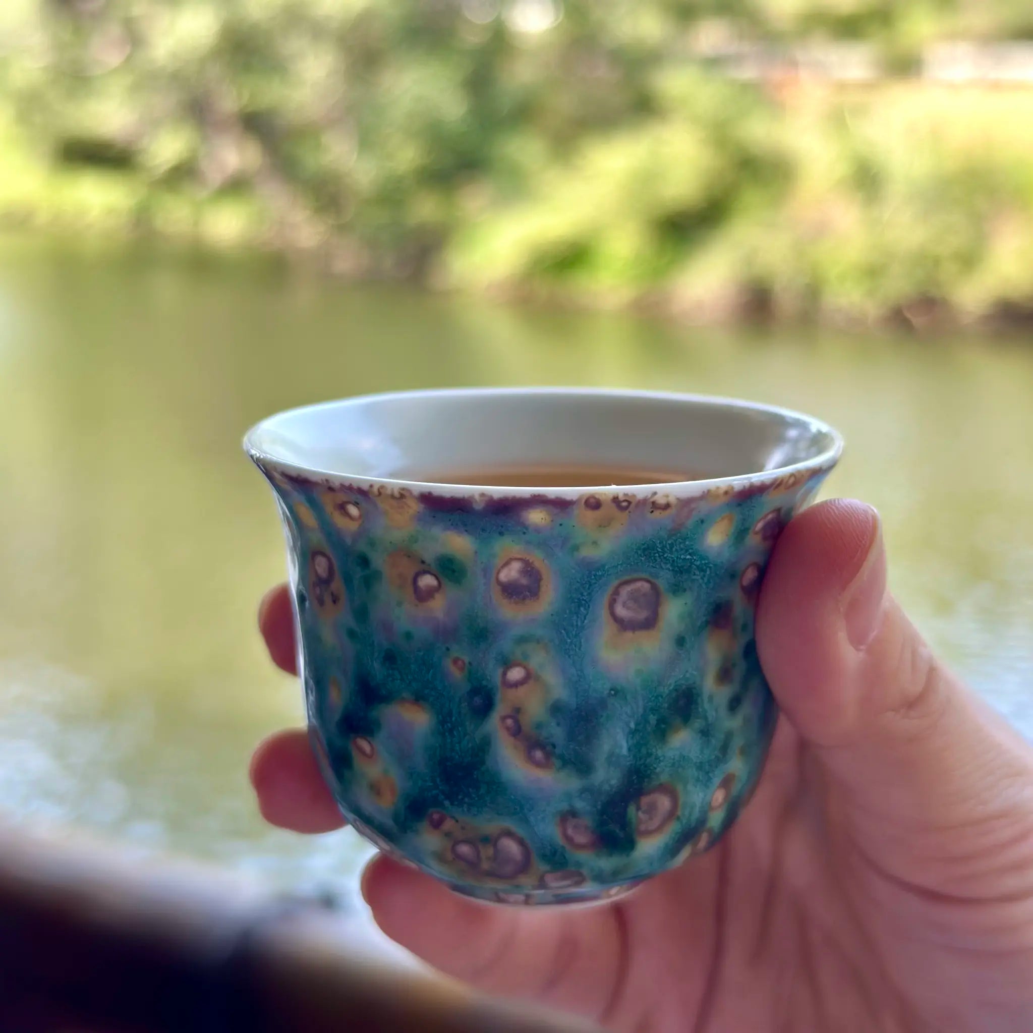Close-up of the 70ml Aurora Shore Elemental master teacup held gently in hand, filled with steeped tea, showcasing the cup's comfortable proportions and striking artisan glaze in a real-world tasting setting.