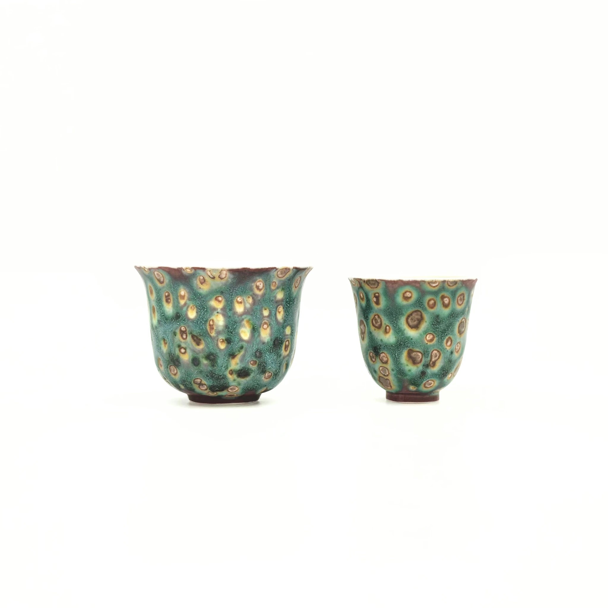 Two ceramic cups with a green and brown speckled pattern on a white background