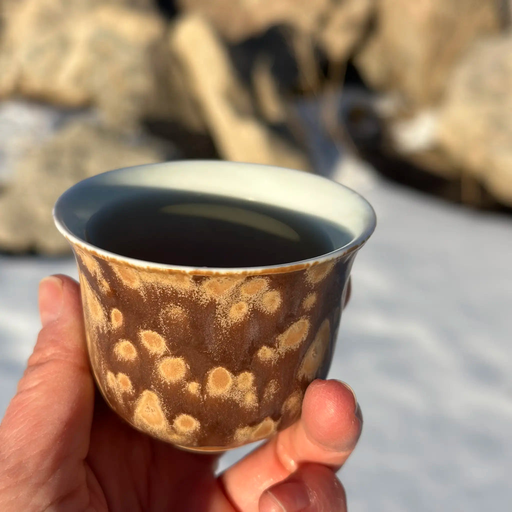 Hand holding a ceramic cup with a textured surface against a rocky background