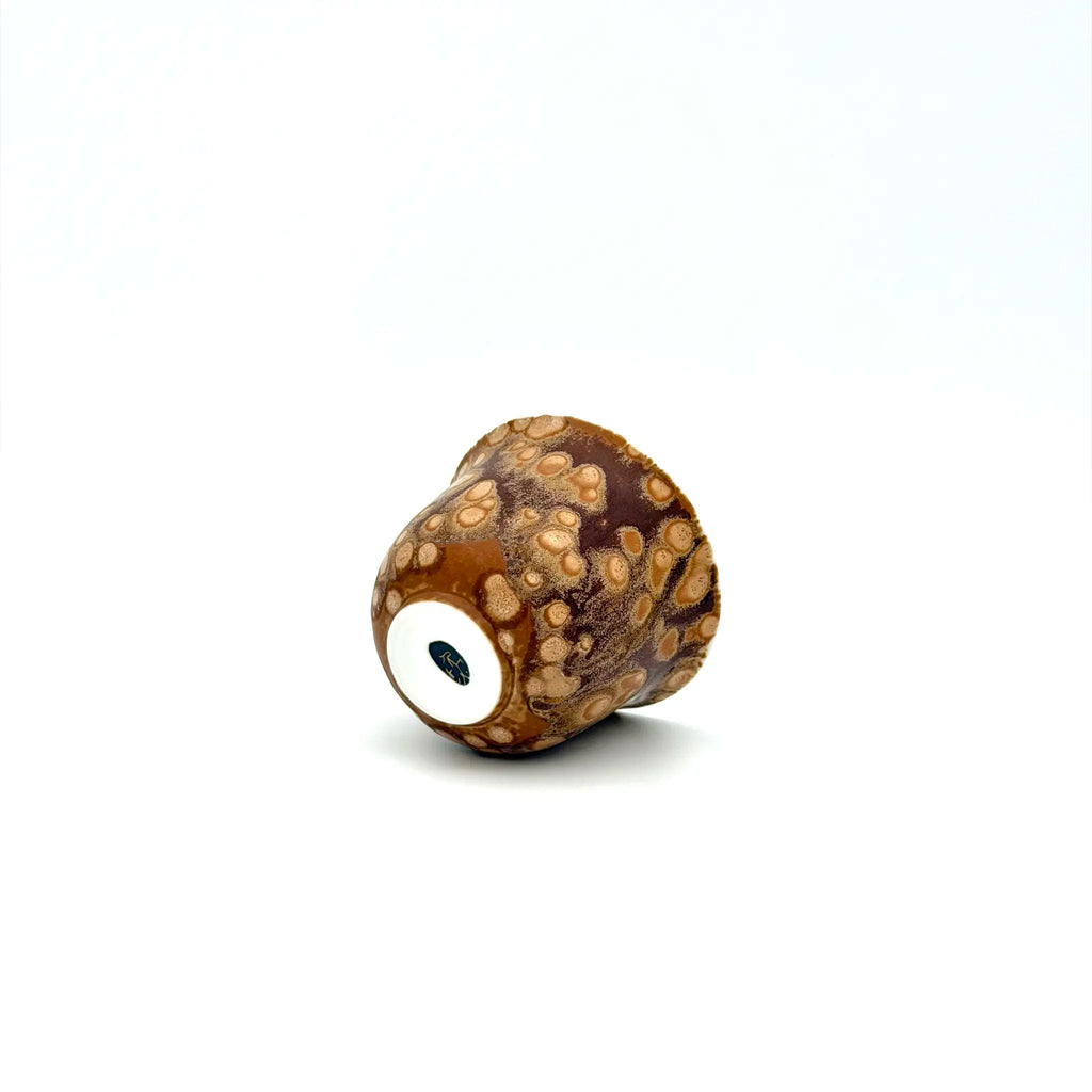 Brown and beige textured cup laying on a white background