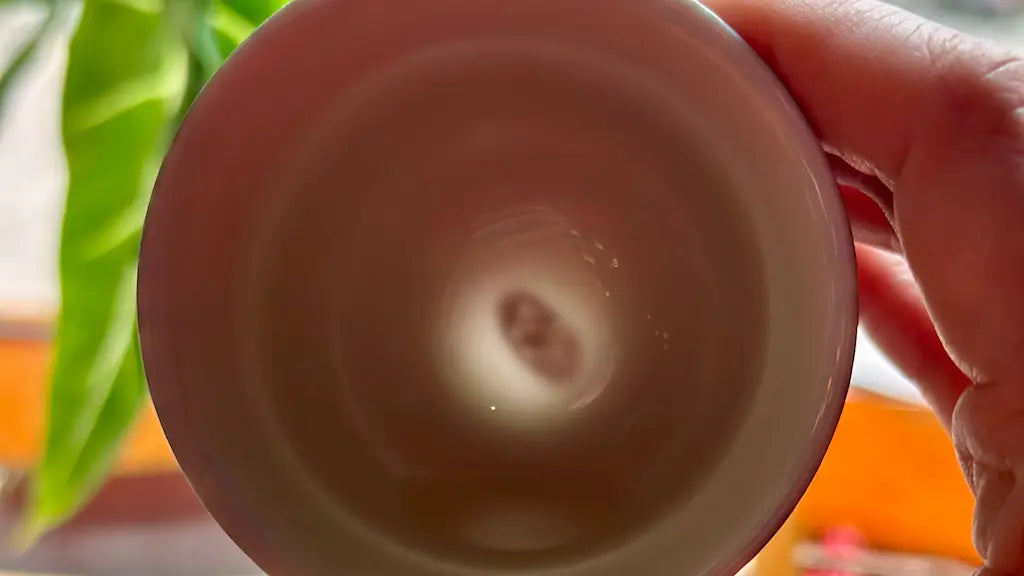 Glazara porcelain teacup held against the light, revealing the hidden artisan's signature at the base through the translucent clay body.