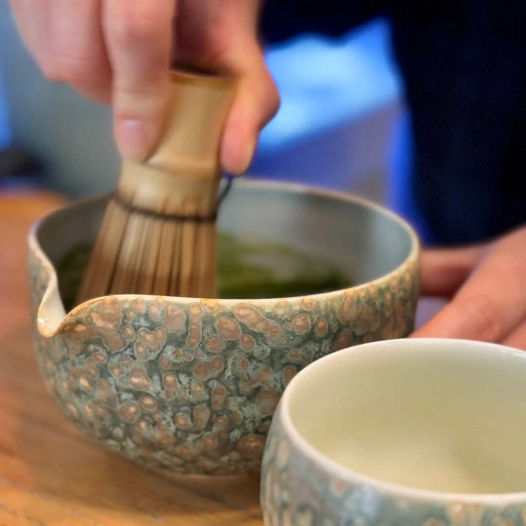 A barista whisking in the Emerald Drift matcha bowl, showcasing its earthy, ocean-inspired ceramic glaze.