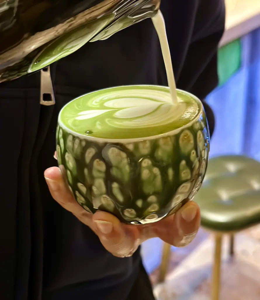 A barista pouring steamed milk into the Glazara Forest Echo matcha latte cup, showcasing the wide, café-style bowl and the cup's earthy, woodland-inspired ceramic glaze.