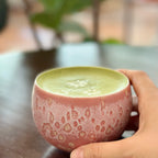 Person holding a pink ceramic cup of matcha latte on a blurred background