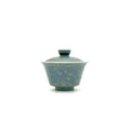 A traditional Chinese gaiwan tea bowl with a matching lid, featuring a speckled blue-green and green glaze on a plain white background.