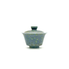 A traditional Chinese gaiwan tea bowl with a matching lid, featuring a speckled blue-green and green glaze on a plain white background.