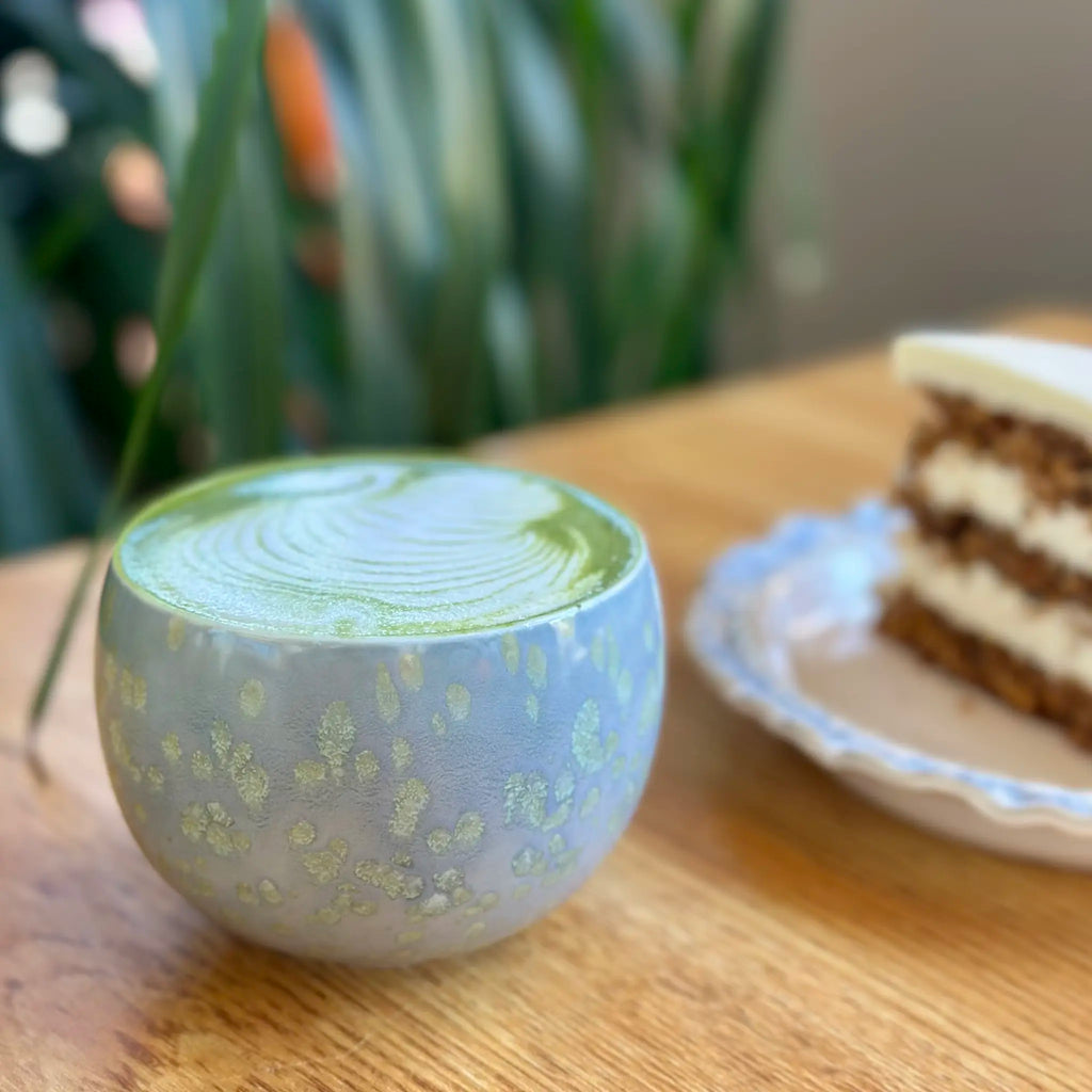 Cup of green matcha latte with a cake on a wooden table