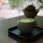 Cup of matcha with latte art on a black tray, blurred background