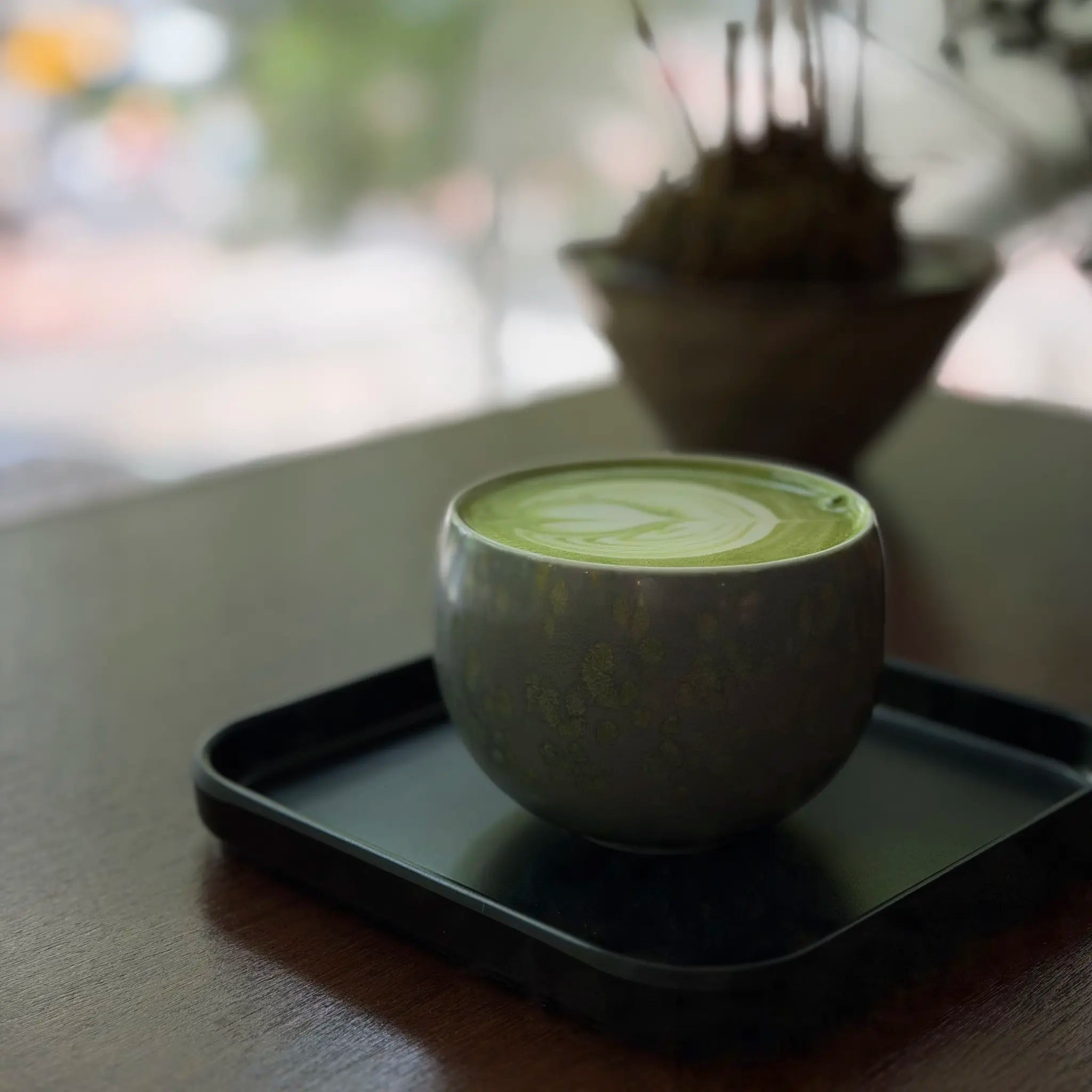 Cup of matcha with latte art on a black tray, blurred background