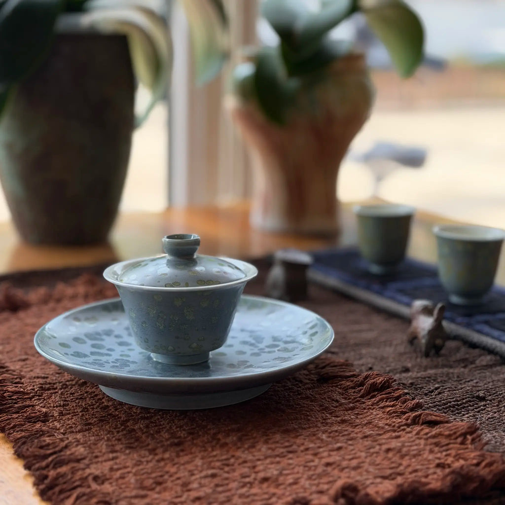 Gaiwan on a tea boat on a tea mat with plants in the background