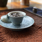 Gaiwan brewing tea leaves sitting on a same-glaze tea boat over a textured tea mat