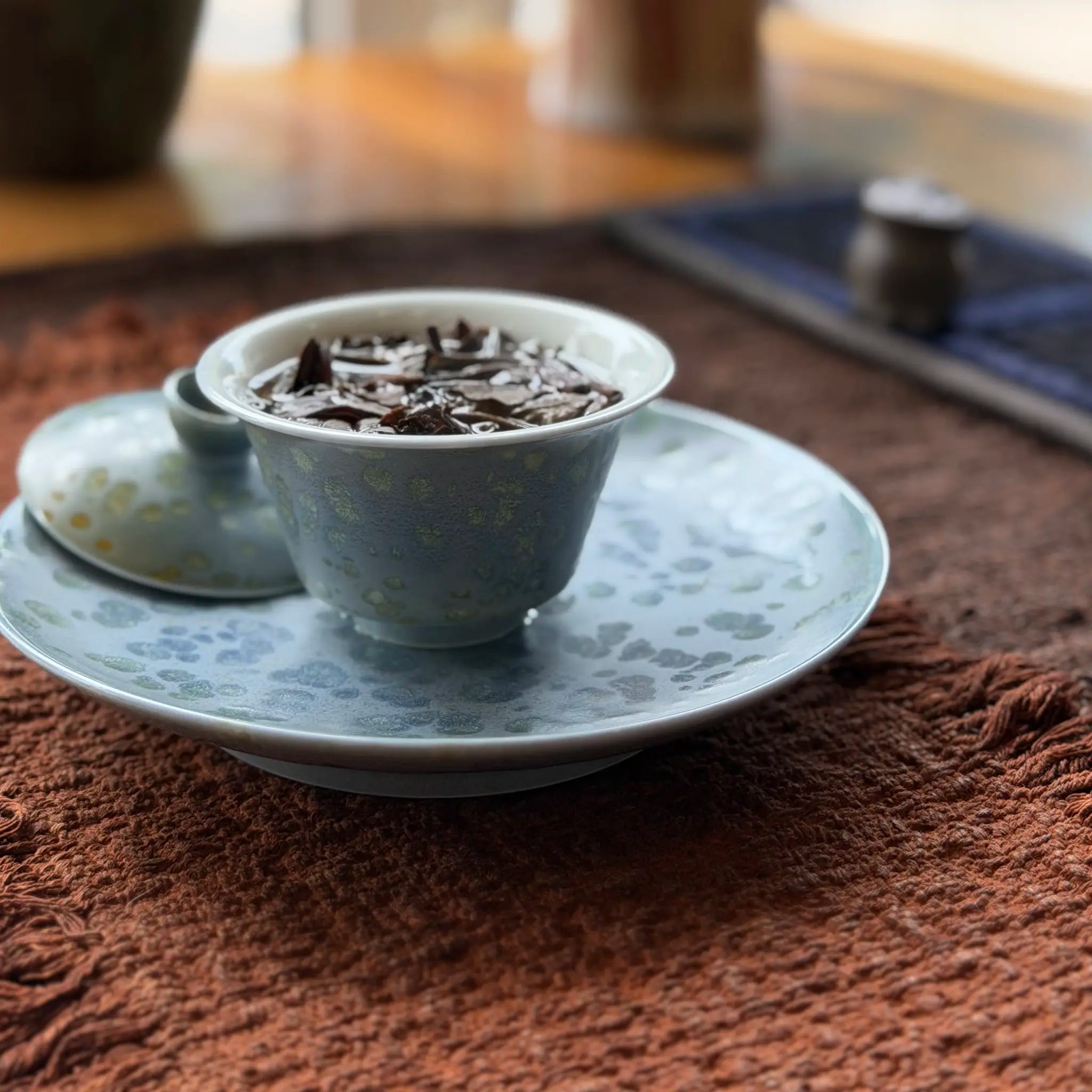 Gaiwan brewing tea leaves sitting on a same-glaze tea boat over a textured tea mat