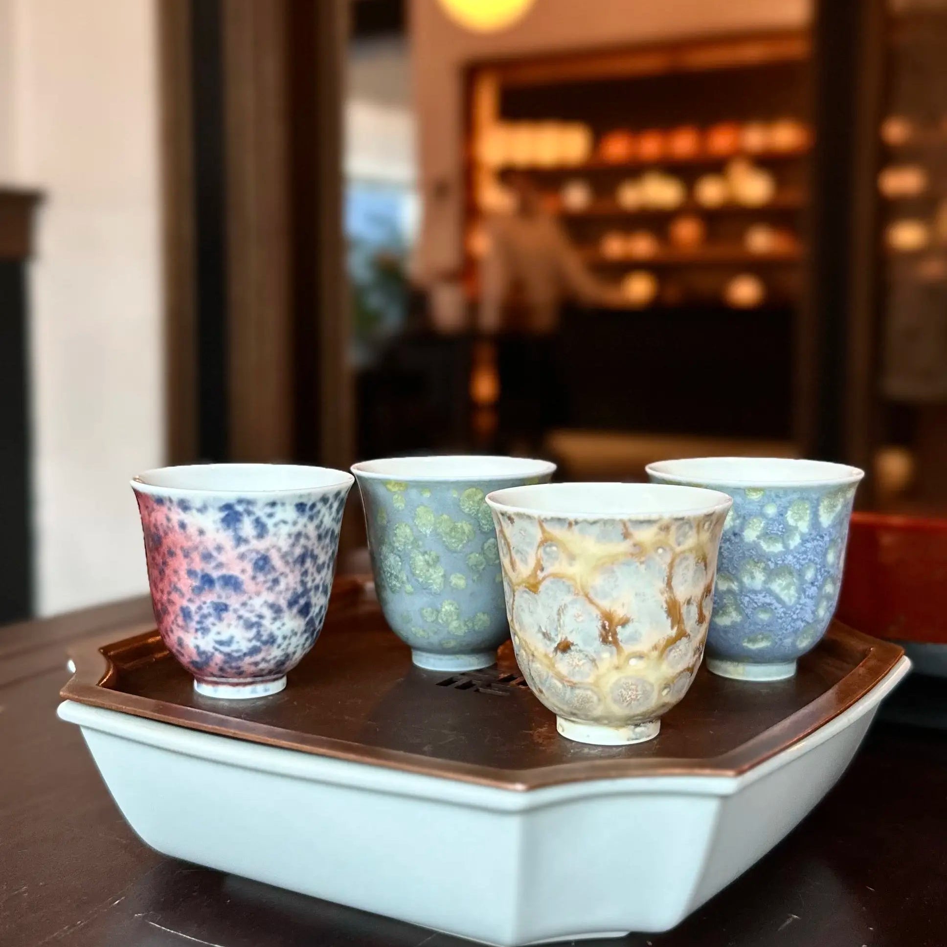 Four patterned cups on a hexagonal white tray with a blurred indoor background