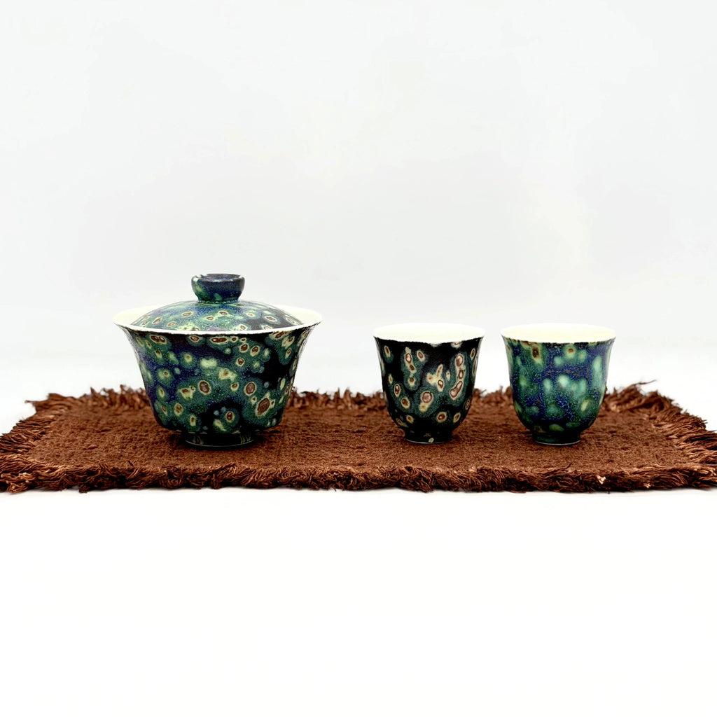Ceramic gaiwan and two cups with minimalism design on a brown tea mat against a white background