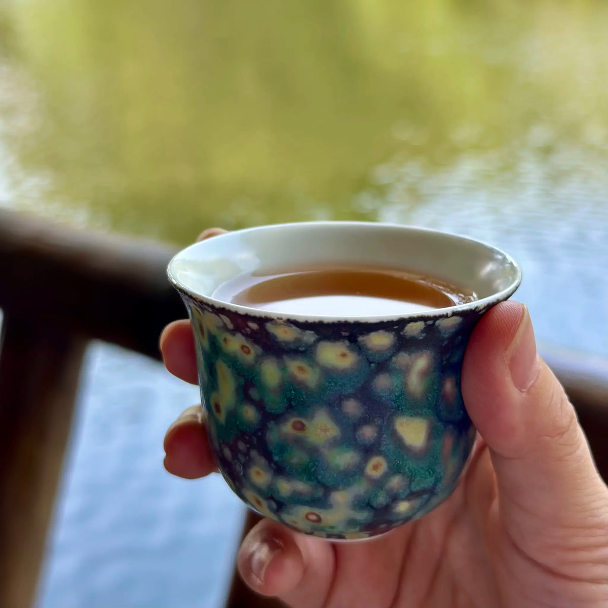 Close-up of the 70ml Midsummer Night Elemental master teacup held gently in hand, filled with steeped tea, showcasing the cup's comfortable proportions and striking artisan glaze in a real-world tasting setting.