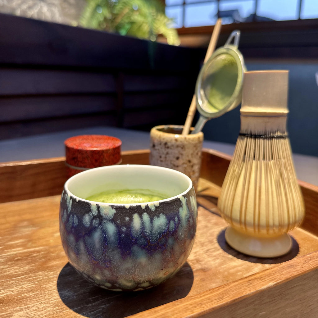A traditional matcha tea ceremony featuring the Glazara Midsummer Night matcha latte cup, showcasing authentic ceremony setting with a bamboo whisk rest beside the deep, twilight-inspired dark ceramic bowl cup.