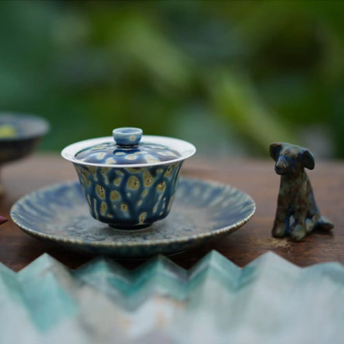 Porcelain gaiwan and tea boat on a wooden surface with a blurred natural background