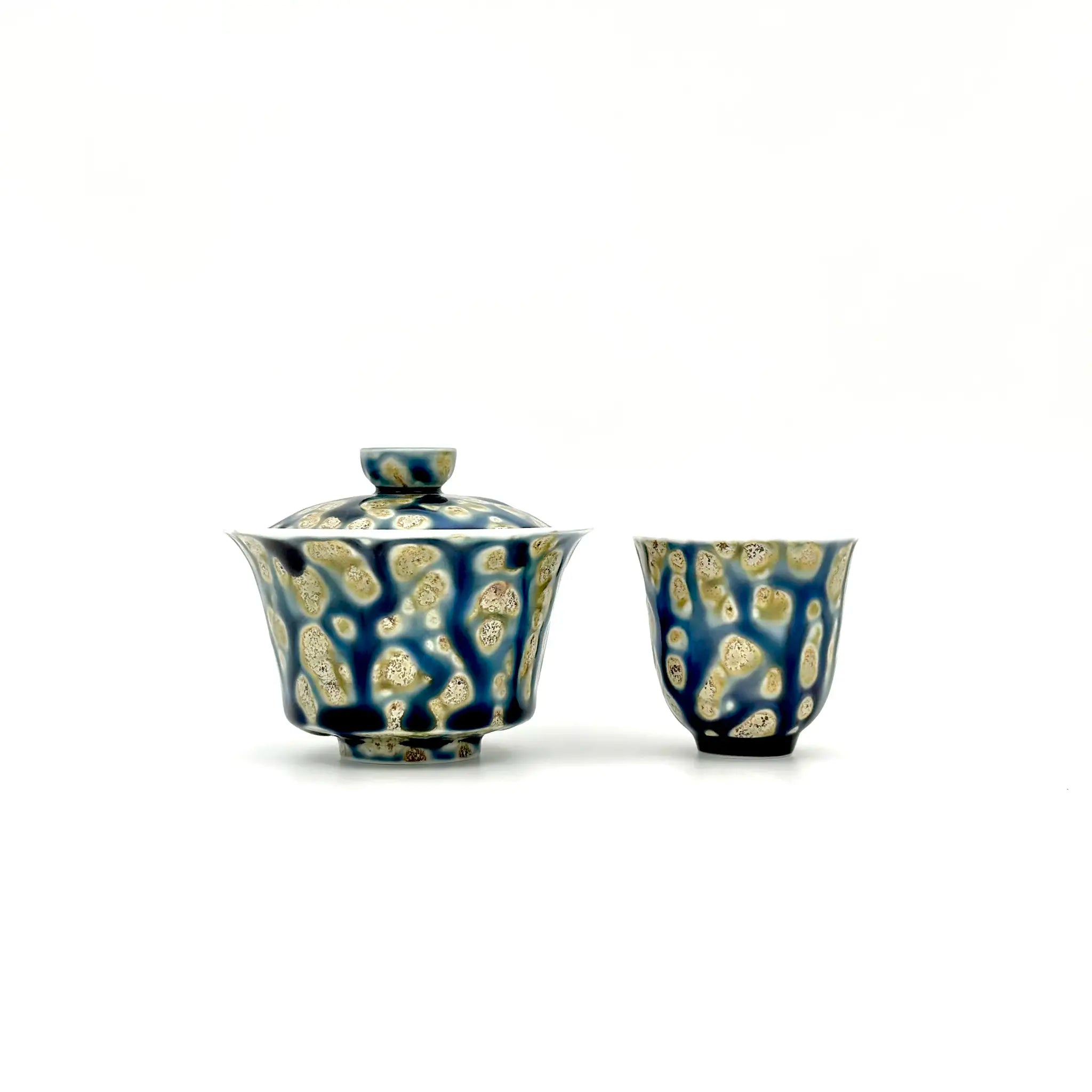 Blue ceramic gaiwan and cup with beige patterns on a white background