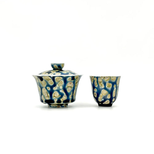 Blue ceramic gaiwan and cup with beige patterns on a white background