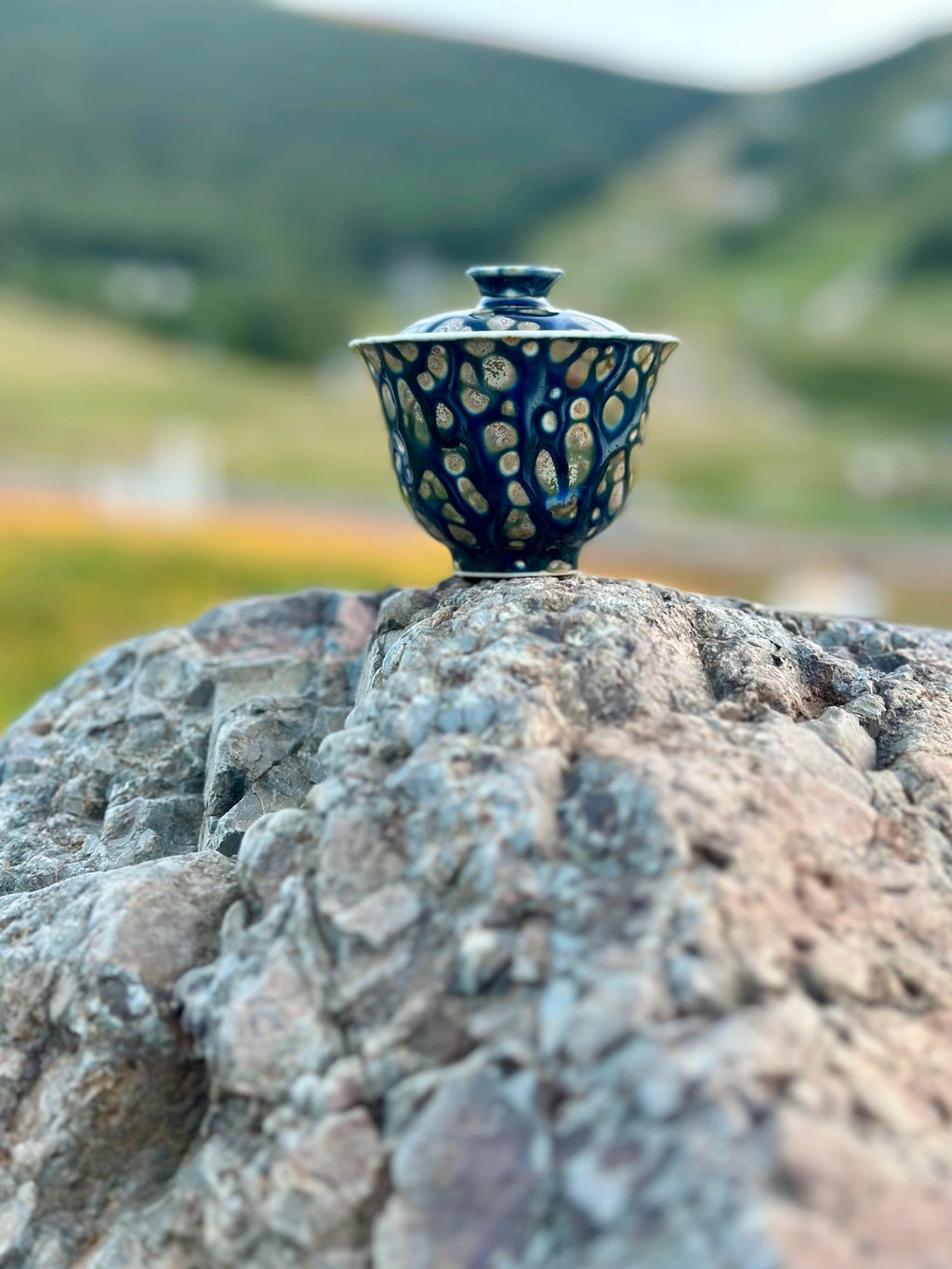 Lifestyle shot of the Ocean Whisper Elemental Gaiwan framed against a scenic mountain landscape. Evokes a serene outdoor tea ceremony atmosphere compatible with travel.