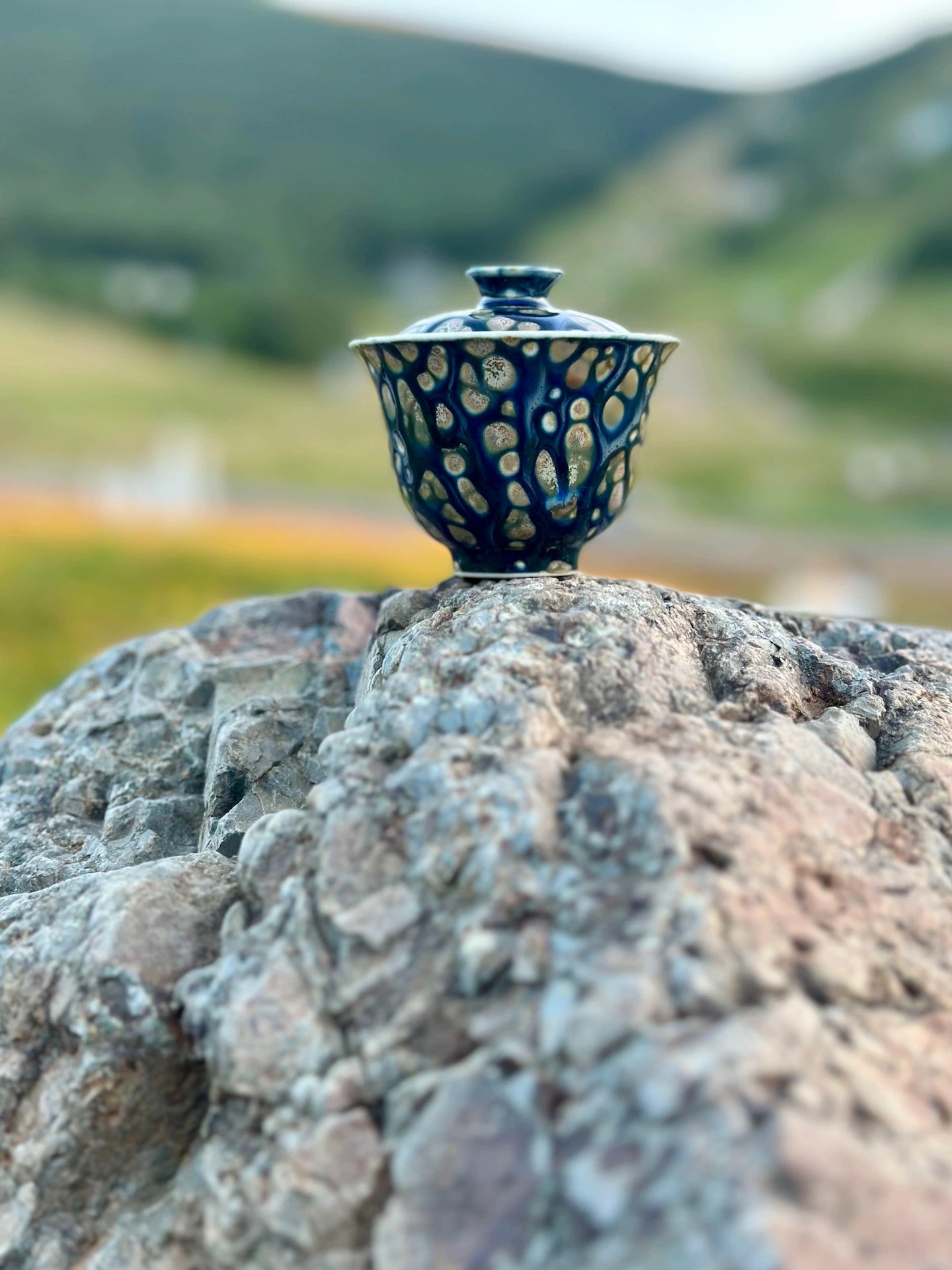 Lifestyle shot of the Ocean Whisper Elemental Gaiwan framed against a scenic mountain landscape. Evokes a serene outdoor tea ceremony atmosphere compatible with travel.