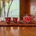 A lifestyle photograph of the Phoenix Spark Chinese Wedding Tea Set, featuring one ceramic gaiwan and two matching tasting teacups resting on a woven tea mat indoors with a softly blurred background.