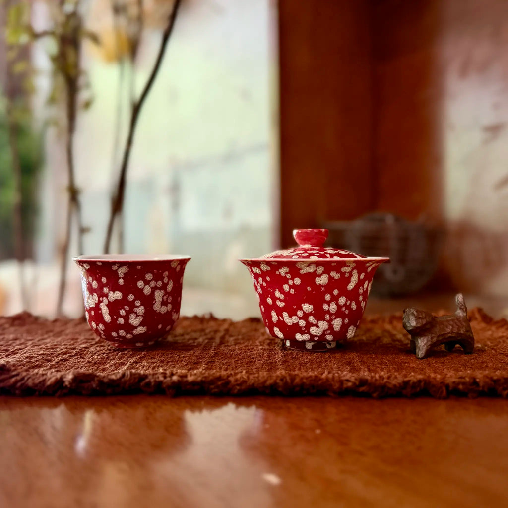 Festive red gaiwan and teacup with light golden dotted patterns on a brown tea mat.