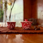 Festive red gaiwan and teacup with light golden dotted patterns on a brown tea mat.