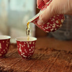 A close-up shot of the Phoenix Spark Chinese wedding gaiwan pouring freshly brewed tea into one of the two matching tasting teacups on a tea mat.