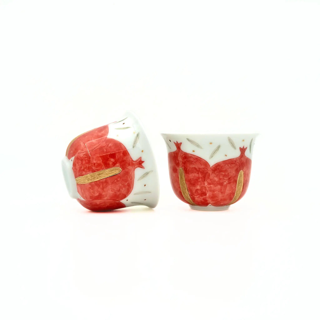 Two ceramic teacups with red pomegranate design on a white background