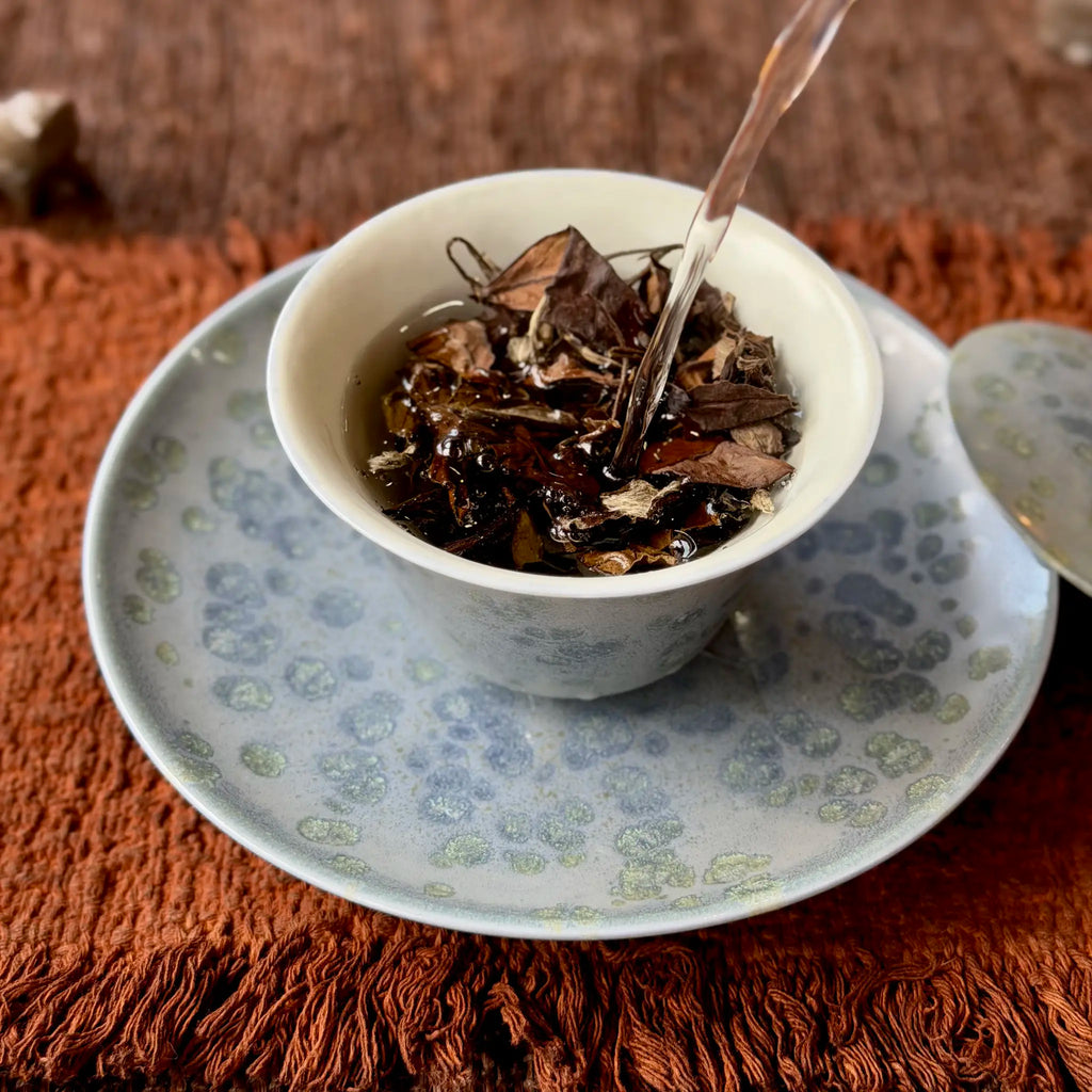 Brewing aged white tea in gaiwan sitting on a matching glaze tea boat, on a textured brown tea mat.