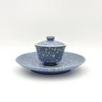 Blue and white ceramic lidded tea bowl set on a matching saucer, photographed against a clean white background.