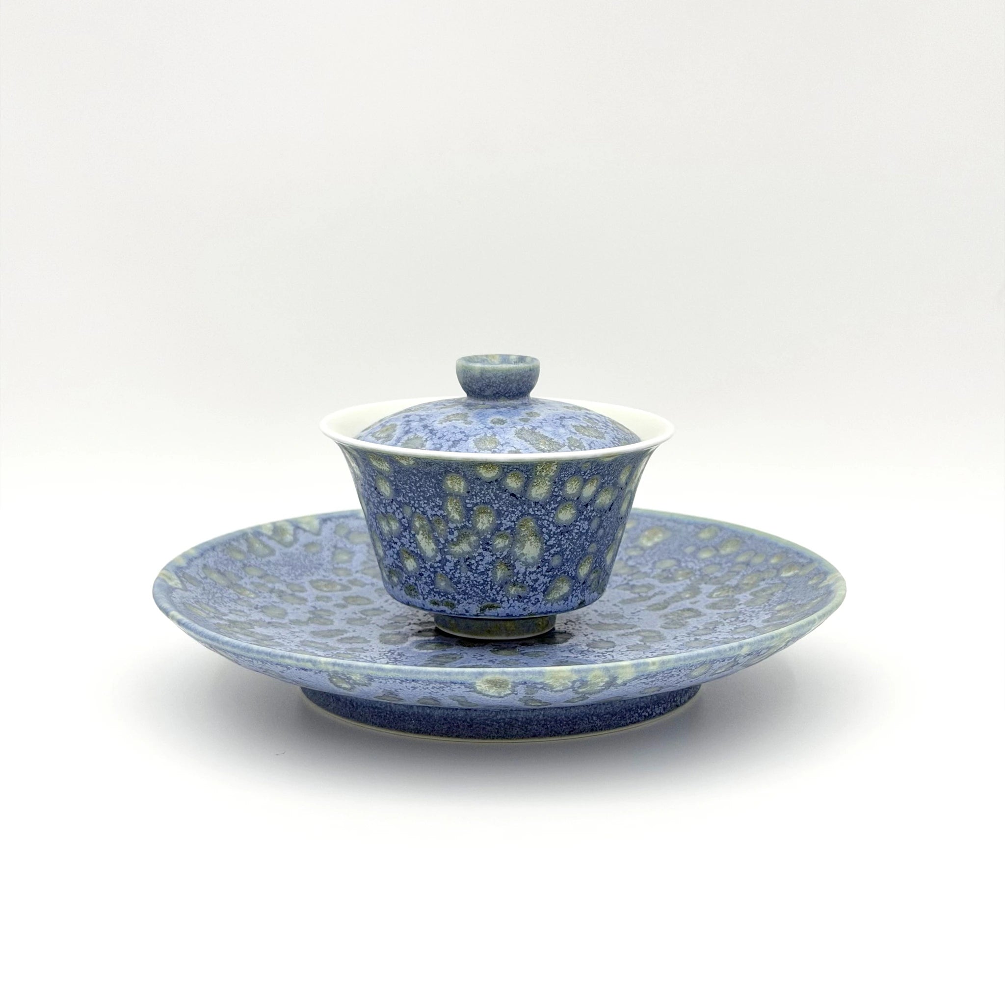 Blue and white ceramic lidded tea bowl set on a matching saucer, photographed against a clean white background.