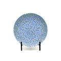 A round ceramic plate with a speckled light blue and white pattern, displayed on a black stand against a white background.