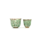 Two green ceramic cups with brown speckles on a white background