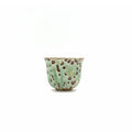 Ceramic teacup with green glaze and brown speckles on a white background