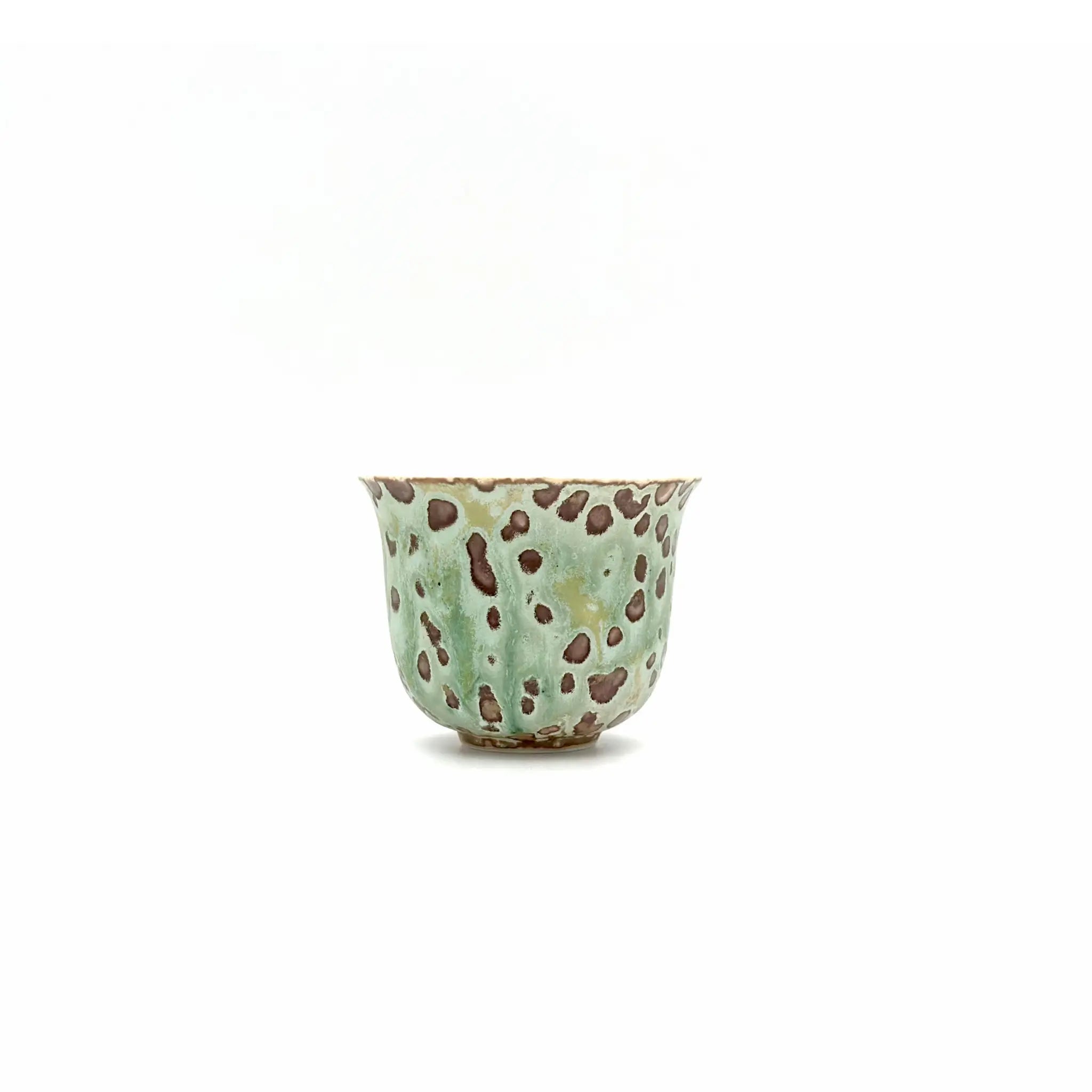 Ceramic teacup with green glaze and brown speckles on a white background