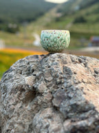 Lifestyle photography of the Sage Dust Matcha Latte Cup placed on natural rock with a blurred mountain backdrop. Emphasizes the cup's rugged durability and its aesthetic connection to nature and outdoor serenity.