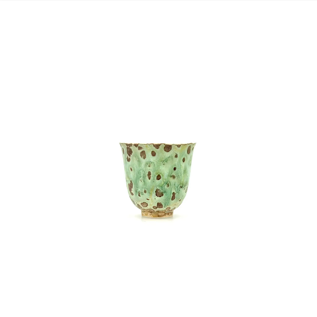 Green ceramic cup with brown speckles on a white background