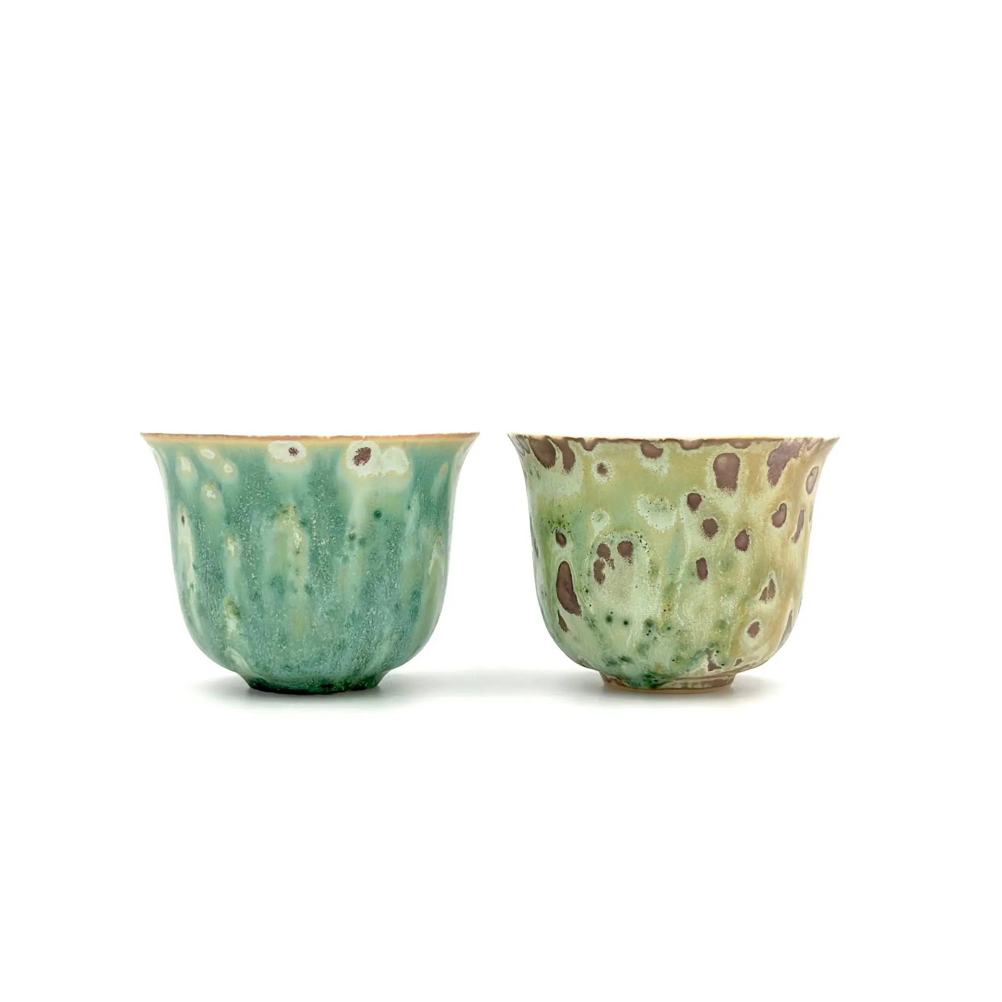 Two ceramic cups with green and brown speckled glaze on a white background