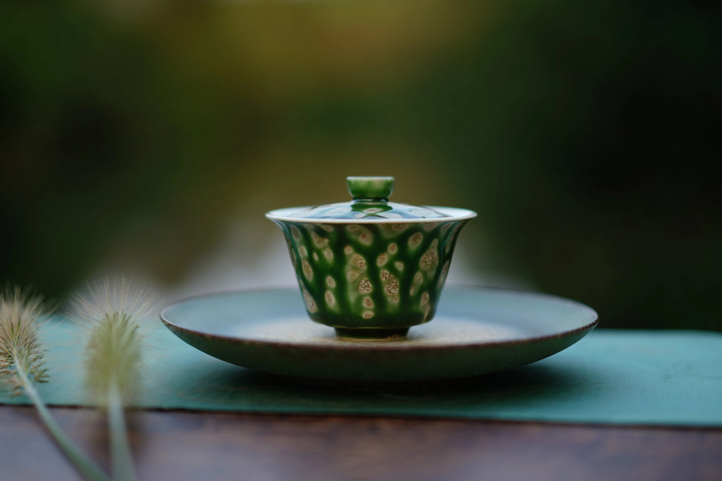 The Glazara Spring Willow Elemental Gaiwan resting elegantly on a green tea boat, framed by an ouutdoor background for an authentic Gongfu tea ceremony setup.