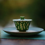 The Glazara Spring Willow Elemental Gaiwan resting elegantly on a green tea boat, framed by an ouutdoor background for an authentic Gongfu tea ceremony setup.