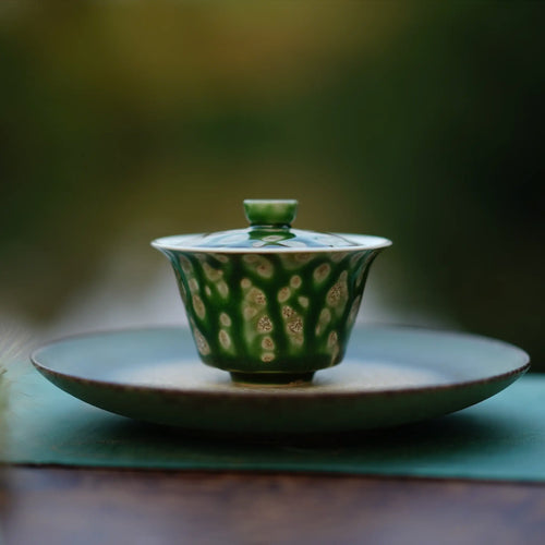 The Glazara Spring Willow Elemental Gaiwan resting elegantly on a green tea boat, framed by an ouutdoor background for an authentic Gongfu tea ceremony setup.
